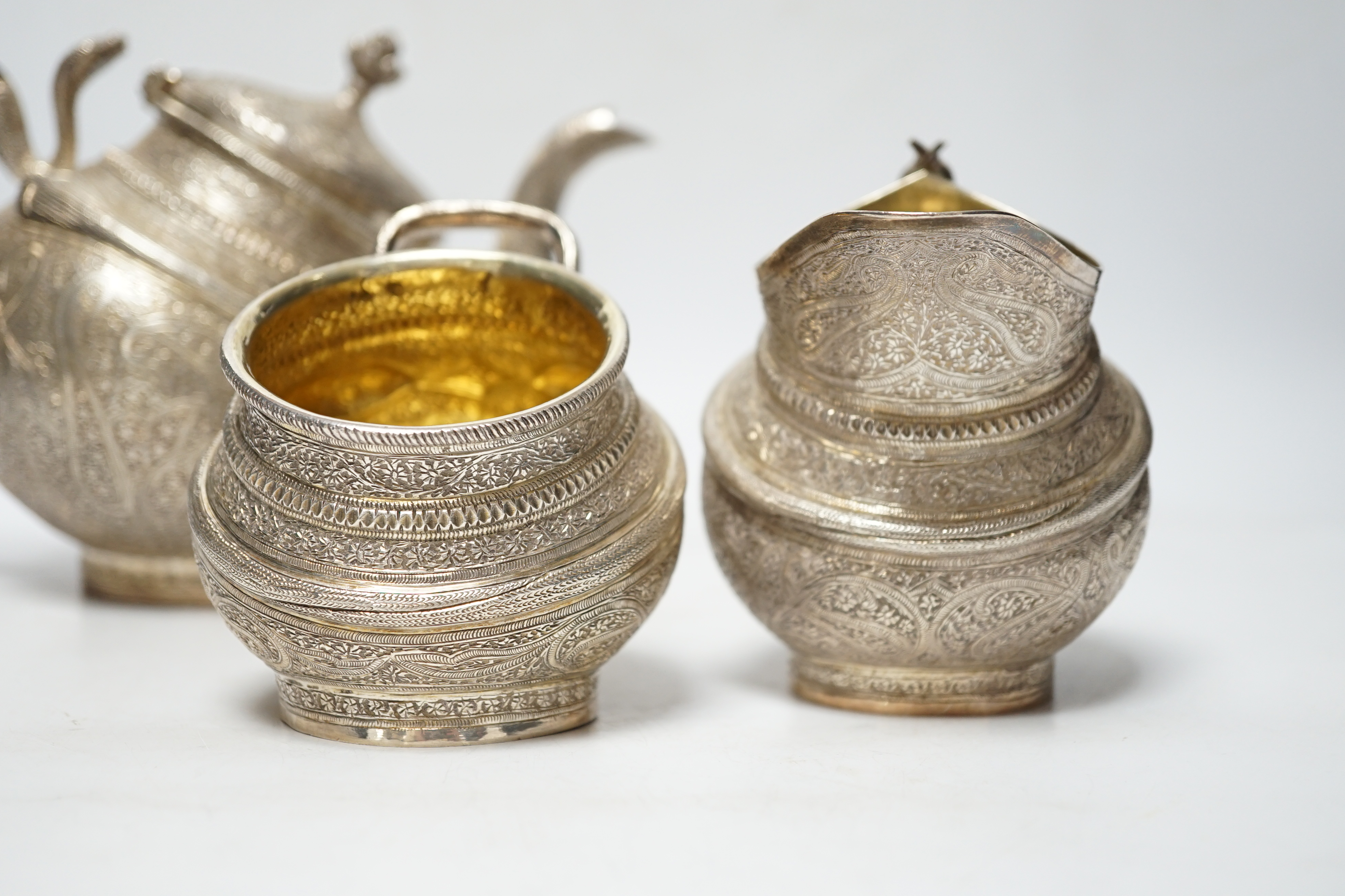 A 20th century Indian three piece embossed white metal tea set, with boteh and cobra decoration, gross weight 38.6oz.